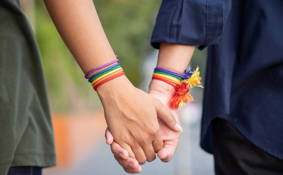 Two people holding hands with rainbow wristbands